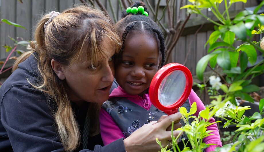 Child and teacher looking through a magnifying glass at a plant