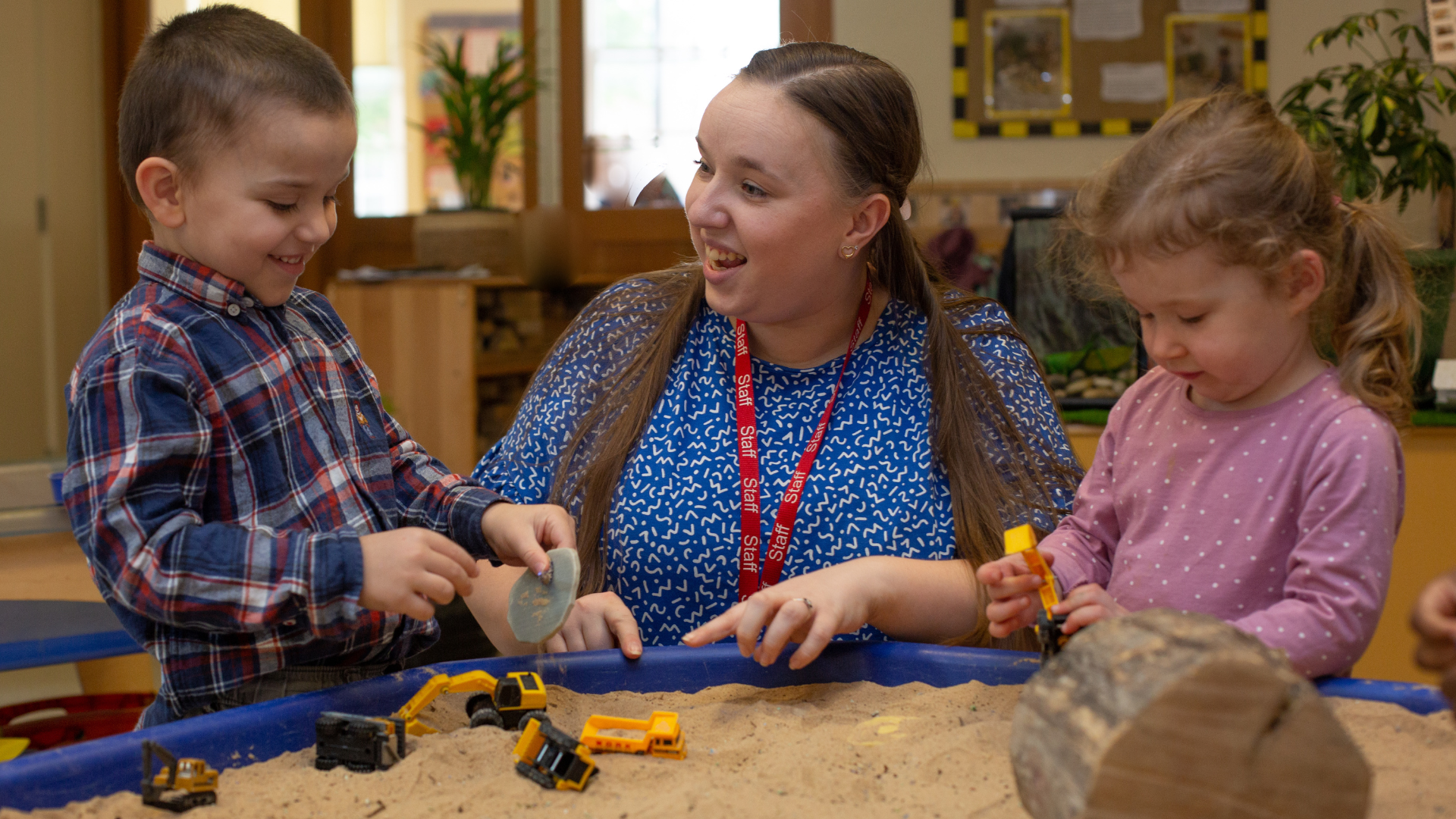 children and staff engaged in an activity using sand and diggers