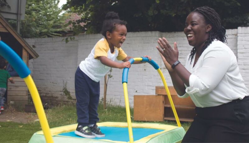 Teacher applauding a laughing child who is bouncing on a trampoline