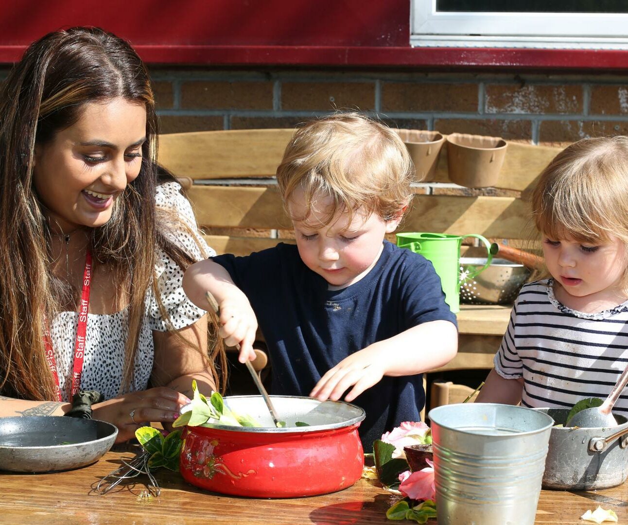 staff and children playing in the outdoor home corner using