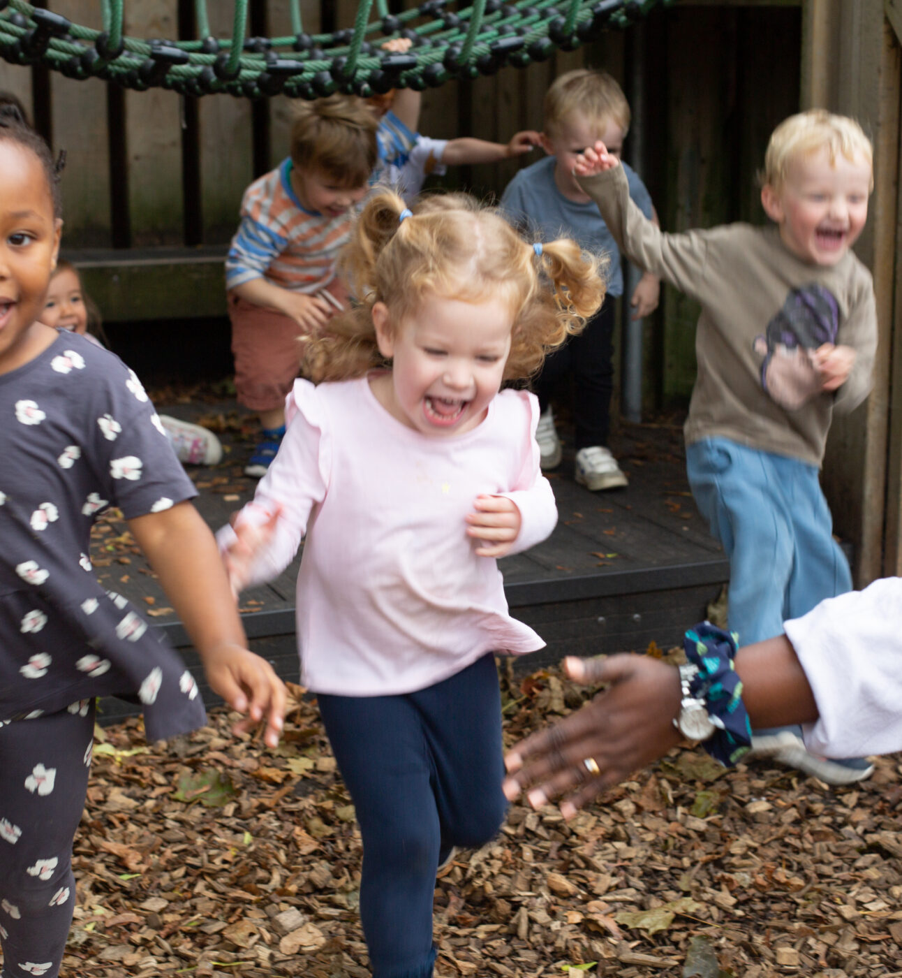 A group of happy smiling children running in the garden playing with a teacher