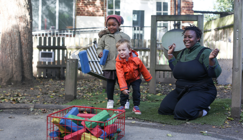 Staff member and two children throwing blocks into a basket