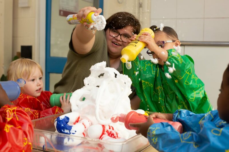 Children and teacher playing with shaving foam and paint