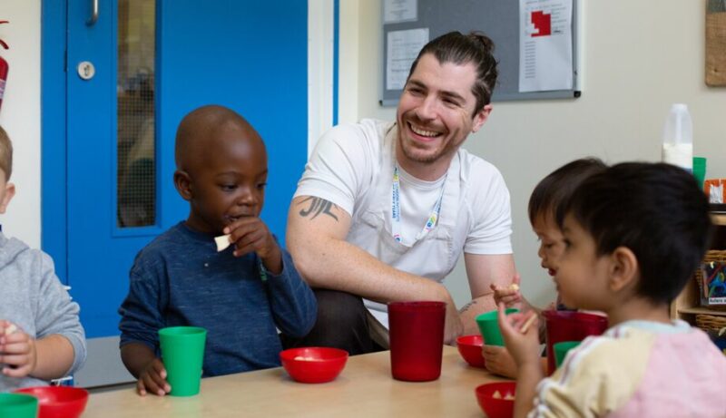 Children eating apple pieces with a smiling LEYF chef